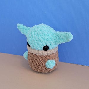 May include: A handmade crochet doll in the likeness of a popular character. The doll features a light blue head with large ears, black eyes, and a brown body. The doll is approximately 5 inches tall.