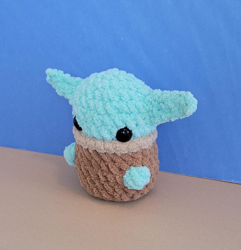 May include: A handmade crochet doll in the likeness of a popular character. The doll features a light blue head with large ears, black eyes, and a brown body. The doll is approximately 5 inches tall.