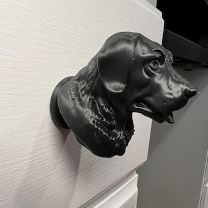 May include: A black, 3D-printed dog head mounted on a white surface. The dog's head is detailed, with visible fur texture and facial features. The dog is a Labrador Retriever.