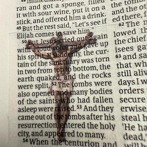 Peut inclure: Un petit crucifix en bois est posé sur un livre ouvert. Le crucifix est brun et détaillé, avec une représentation de Jésus. Les pages du livre sont jaunies et le texte est visible. L'image est une représentation religieuse.