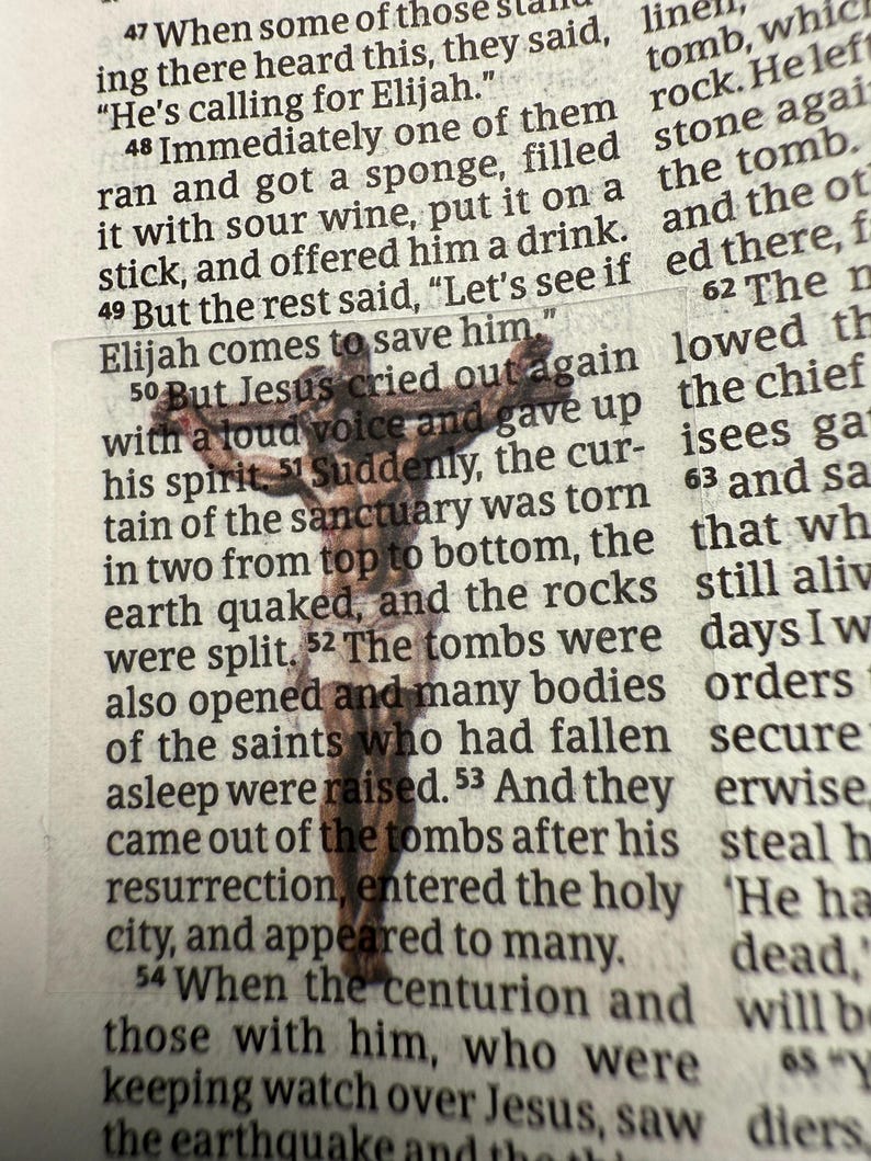 Puede incluir: Un peque&ntilde;o crucifijo de madera se encuentra sobre un libro abierto. El crucifijo es marr&oacute;n y detallado, con una figura de Jes&uacute;s. Las p&aacute;ginas del libro est&aacute;n amarillentas y el texto es visible. La imagen es una representaci&oacute;n religiosa.
