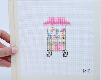 May include: A pink and white candy cart with colorful candies and a pink roof. The cart has two black wheels and the initials "ML" are printed on the bottom right corner.