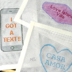 Puede incluir: Tres lienzos blancos para bordar. Uno presenta un smartphone pixelado con las palabras "I GOT A TEXT!!" en naranja. Otro tiene un bocadillo rosa y morado con "Love Island Villa". El tercero tiene un coraz&oacute;n azul con "Casa Amor".