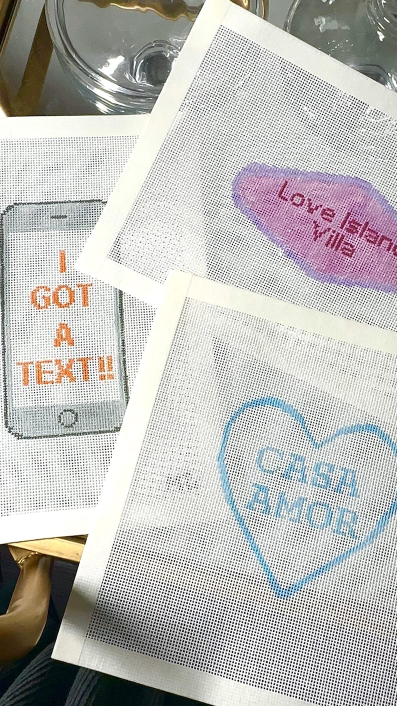 Puede incluir: Tres lienzos blancos para bordar. Uno presenta un smartphone pixelado con las palabras "I GOT A TEXT!!" en naranja. Otro tiene un bocadillo rosa y morado con "Love Island Villa". El tercero tiene un coraz&oacute;n azul con "Casa Amor".