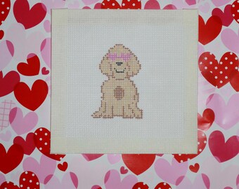May include: A beige dog with pink glasses is sitting on a white canvas. The canvas is surrounded by a pink and red heart pattern.