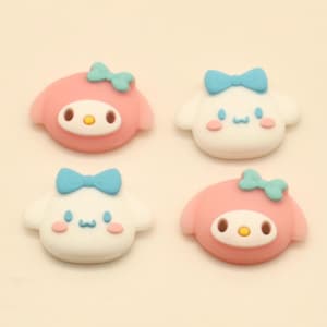 May include: Four cartoon character embellishments. Two are pink with blue bows, and two are white with blue bows. Each has a face with eyes and a mouth. The embellishments are on a cream-colored background. The text "ArtisanGlowCoCrafts" is at the bottom.