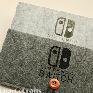 May include: Two gray felt Nintendo Switch cases. The top case is light gray with the Nintendo logo. The bottom case is dark gray with the Nintendo Switch logo and an orange button closure.