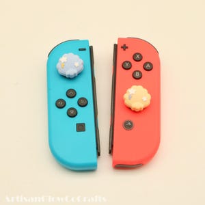 May include: A pair of Nintendo Switch Joy-Con controllers, one blue and one red. Each controller has a decorative cloud charm with star accents. The blue controller has black buttons and a black joystick. The red controller has black buttons and a black joystick.