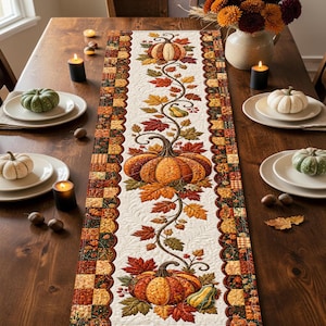 May include: A rectangular fabric table runner featuring a central cream-coloured panel decorated with a vertical vine pattern of orange pumpkins, green gourds, and multicoloured autumn leaves, bordered by a patchwork design of fall-themed squares.