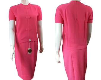 May include: A pink two-piece knit dress with a short-sleeved top and a skirt. The top has a mock neck and a row of buttons down the front. The skirt is a-line and falls to the knees.