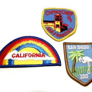 May include: Three embroidered patches: a rainbow with "CALIFORNIA" text, a shield with a San Francisco Chinatown scene, and a shield with a San Diego Zoo flamingo and palm tree design.