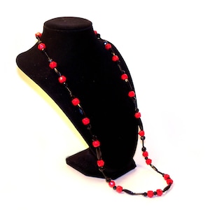 May include: A black necklace with red beads on a black mannequin bust.