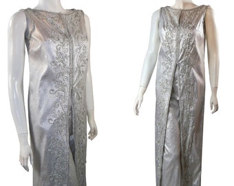 May include: A silver jumpsuit with a long, flowing top and pants. The top has a V-neckline and is decorated with silver embroidery. The pants are wide-legged and have a straight leg.