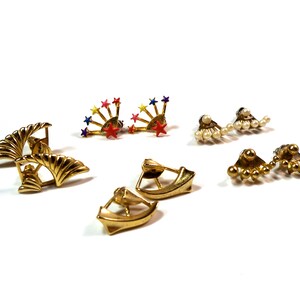 May include: Assortment of gold tone earrings with various designs. Some earrings feature a fan shape, others have a row of small balls, and some have a starburst design with colorful enamel.