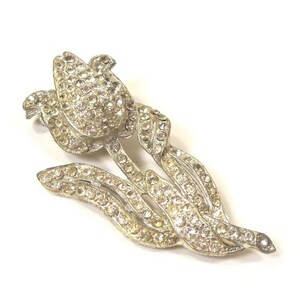 May include: A silver-toned brooch in the shape of a tulip with clear rhinestones. The brooch has a single tulip with a stem and leaves.