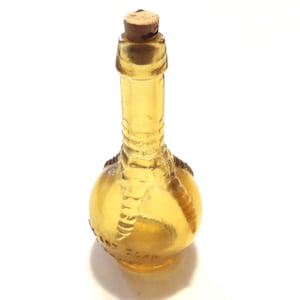 Könnte beinhalten: Eine gelbe Glasflasche mit einem Vogelklauen-Design am Boden und einem Korken. Die Flasche hat einen abgerundeten Boden und einen langen Hals. Das Glas hat eine transparente Bernsteinfarbe.