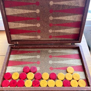 May include: Open vintage backgammon set with red and yellow game pieces. The game board is brown with red and white triangular markings. The set is in a brown case with a clasp.