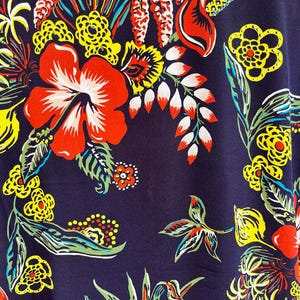 Peut inclure: Gros plan sur un tissu bleu marine avec un motif floral vif. Le design pr&eacute;sente de grandes fleurs d'hibiscus rouges, des fleurs jaunes et des feuilles vertes, accentu&eacute;es de d&eacute;tails blancs et orange. L'esth&eacute;tique g&eacute;n&eacute;rale est tropicale et color&eacute;e.