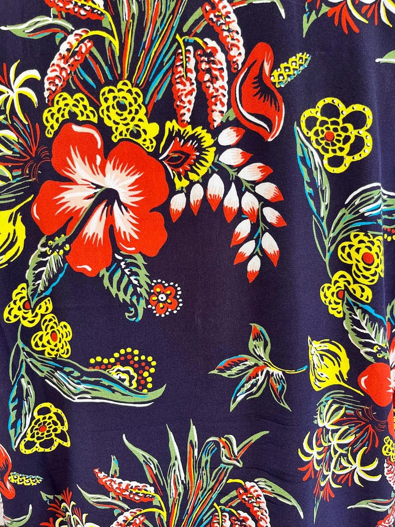 Peut inclure: Gros plan sur un tissu bleu marine avec un motif floral vif. Le design pr&eacute;sente de grandes fleurs d'hibiscus rouges, des fleurs jaunes et des feuilles vertes, accentu&eacute;es de d&eacute;tails blancs et orange. L'esth&eacute;tique g&eacute;n&eacute;rale est tropicale et color&eacute;e.