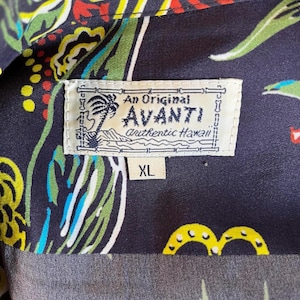 Peut inclure: Gros plan sur une chemise hawa&iuml;enne bleu fonc&eacute; avec un motif floral color&eacute;. La chemise porte une &eacute;tiquette indiquant "An Original Avanti authentic Hawaii" et la taille "XL". Le motif de la chemise comprend des touches de rouge, jaune, vert et bleu.