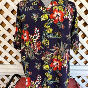 Peut inclure: Chemise bleu marine &agrave; motifs floraux color&eacute;s. Le motif pr&eacute;sente de grandes fleurs d'hibiscus rouges, des accents jaunes et du feuillage vert. La chemise a des manches courtes et un col classique, id&eacute;ale pour une tenue d&eacute;contract&eacute;e.