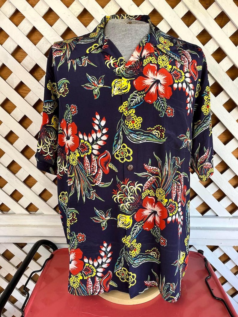 Peut inclure: Chemise bleu marine &agrave; motifs floraux color&eacute;s. Le motif pr&eacute;sente de grandes fleurs d'hibiscus rouges, des accents jaunes et du feuillage vert. La chemise a des manches courtes et un col classique, id&eacute;ale pour une tenue d&eacute;contract&eacute;e.