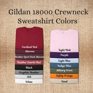 May include: Image showing a selection of Gildan 18000 crewneck sweatshirt colors. Colors include Cardinal Red, Maroon, Heather Sport Dark Maroon, Heather Scarlet Red, Black, Graphite Heather, Ash, White, Light Pink, Purple, Light Blue, Indigo Blue, Military Green, Safety Orange, and Sand.