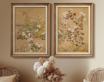 May include: Two framed floral art prints. Each print features a botanical illustration of white flowers, green leaves, and tall grasses against a tan background. The frames are light brown with a white inner border.