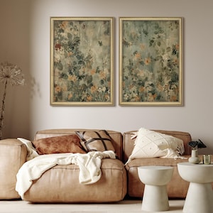 May include: Two framed floral art prints with gold frames hang above a brown leather sofa. The artwork features a muted color palette of greens, oranges, and whites. Decorative pillows and a cream-colored throw blanket adorn the sofa.