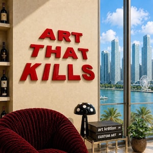 May include: A wall display featuring the red three-dimensional text ART THAT KILLS, positioned above a black mushroom-shaped lamp, two stacked books titled art kr8tion and CUSTOM ART, and a deep red textured armchair in a room with a city view.
