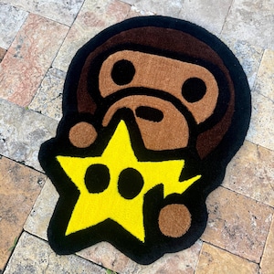 Puede incluir: Una alfombra personalizada con la cabeza de un mono de dibujos animados con una estrella amarilla. La alfombra tiene una combinación de colores marrón, negro y amarillo. La alfombra está colocada sobre una superficie de baldosas de piedra.