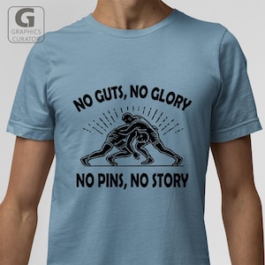 May include: A light blue t-shirt with a black graphic of two wrestlers. The text "NO GUTS, NO GLORY NO PINS, NO STORY" is printed on the shirt.