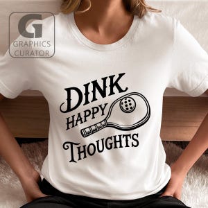 May include: White t-shirt with black text that reads "Dink Happy Thoughts" and a black and white illustration of a pickleball paddle.