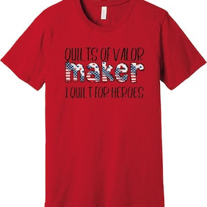 May include: Red t-shirt with the text "Quilts of Valor maker I quilt for heroes" in black. The word "maker" is decorated with an American flag pattern.