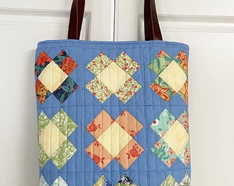 May include: A blue quilted tote bag with brown leather straps. The bag is decorated with a patchwork design of colorful squares.