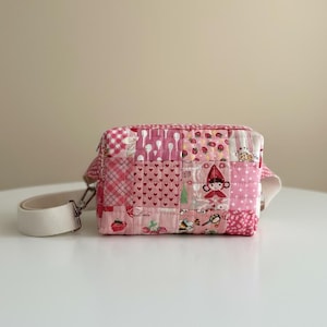 May include: A pink patchwork crossbody bag with a white strap. The bag features various pink patterns, including hearts, strawberries, and a Little Red Riding Hood design. The bag has a rectangular shape and a silver metal clasp.