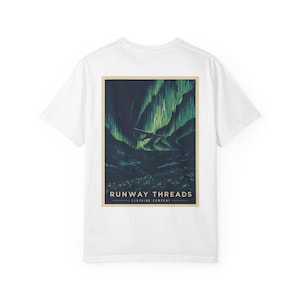 Op de afbeelding: Wit T-shirt met een rechthoekige afbeelding op de achterkant met een landschap met groene en blauwe tinten, mogelijk het noorderlicht. De tekst "RUNWAY THREADS CLOTHING COMPANY" staat onder de afbeelding.