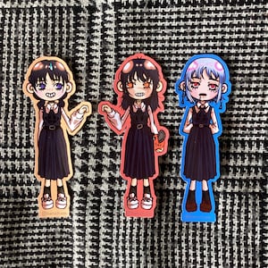 Puede incluir: Tres pegatinas de estilo anime con personajes vestidos con vestidos negros y camisas blancas. Las pegatinas tienen contornos melocotón, rojos y azules. Cada personaje tiene colores de pelo y ojos únicos. Las pegatinas están sobre un fondo con estampado en blanco y negro.