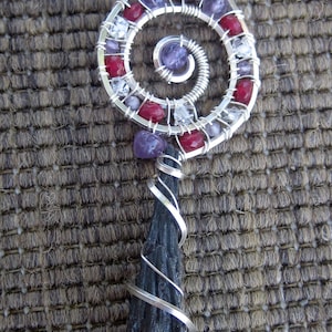 May include: A silver wire wrapped pendant with a black stone and a spiral design featuring red, purple, and clear gemstones.