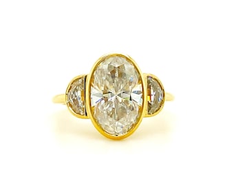 Può includere: Un anello d'oro con un diamante centrale di taglio ovale, affiancato da due diamanti più piccoli a forma di mezzaluna. I diamanti sono incastonati in una montatura a castone e la fascia è in oro lucido.
