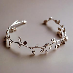 May include: A silver-toned metal headband with a delicate leaf and vine design. The leaves are intricately detailed, and the headband has an open design. This piece is suitable for weddings, special occasions, or everyday wear.