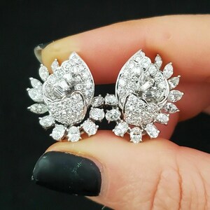 May include: A pair of silver-toned earrings featuring a cluster of round, marquise, and baguette-cut clear stones. The design includes a central heart-shaped section surrounded by a fan-like arrangement of various stone shapes and sizes.