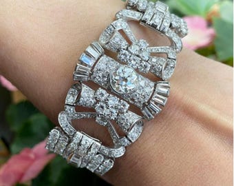 May include: A dazzling diamond bracelet featuring a central round-cut diamond surrounded by smaller stones and baguette-cut diamonds. The bracelet has an intricate design with a silver-colored metal setting, showcasing a luxurious and elegant style.