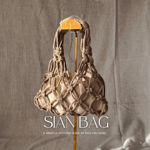 Może przedstawiać: Beżowa torba z makramy z tkanym wzorem siatki, z kremowym wnętrzem. Torba ma wiązany uchwyt i jest prezentowana na złotym stojaku. Widoczny jest tekst "SIAN BAG" i "A MINDFUL PATTERN GUIDE BY MISS MACREBEL".