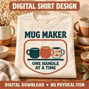 May include: A cream-coloured t-shirt featuring a graphic with the text MUG MAKER and ONE HANDLE AT A TIME. The design includes three illustrated mugs in dark blue, terracotta, and white with a geometric pattern, all enclosed in a rounded frame.