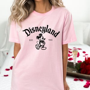 May include: Pink t-shirt with a black graphic of Mickey Mouse and the text "Disneyland Est. 1955"