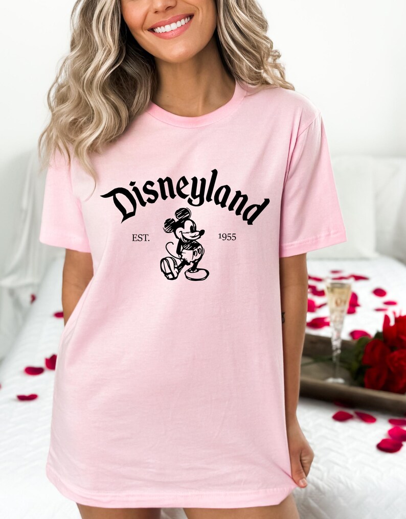May include: Pink t-shirt with a black graphic of Mickey Mouse and the text "Disneyland Est. 1955"