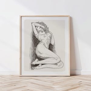 Könnte beinhalten: Gerahmte Federzeichnung einer nackten Figur in liegender Pose. Das Kunstwerk zeigt detaillierte Schattierungen und Linien, wobei die Form der Figur vor einem neutralen Hintergrund hervorgehoben wird. Der Rahmen ist hellholzfarben.
