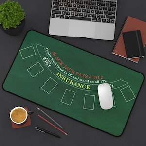 May include: A green rectangular mouse mat featuring a blackjack table design. The text "BLACK JACK PAYS 3 TO 2" and "INSURANCE" is visible. A white computer mouse sits on the mat, along with a laptop, notebook, and a cup of coffee.