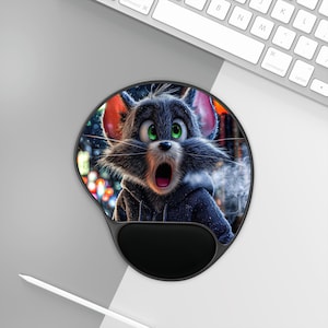 May include: A black and gray ergonomic mouse pad featuring a cartoon cat with wide green eyes and an open mouth. The cat is wearing a dark gray hoodie. The mouse pad has a black wrist rest and is on a white and gray surface.